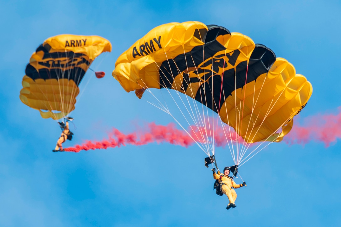 Two soldiers free fall with parachutes surrounded by red smoke.