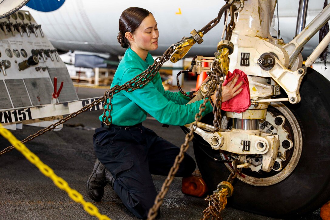 A sailor wipes down an aircraft wheel.