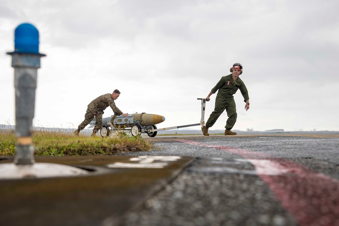 Two Marines use equipment to move a munition.