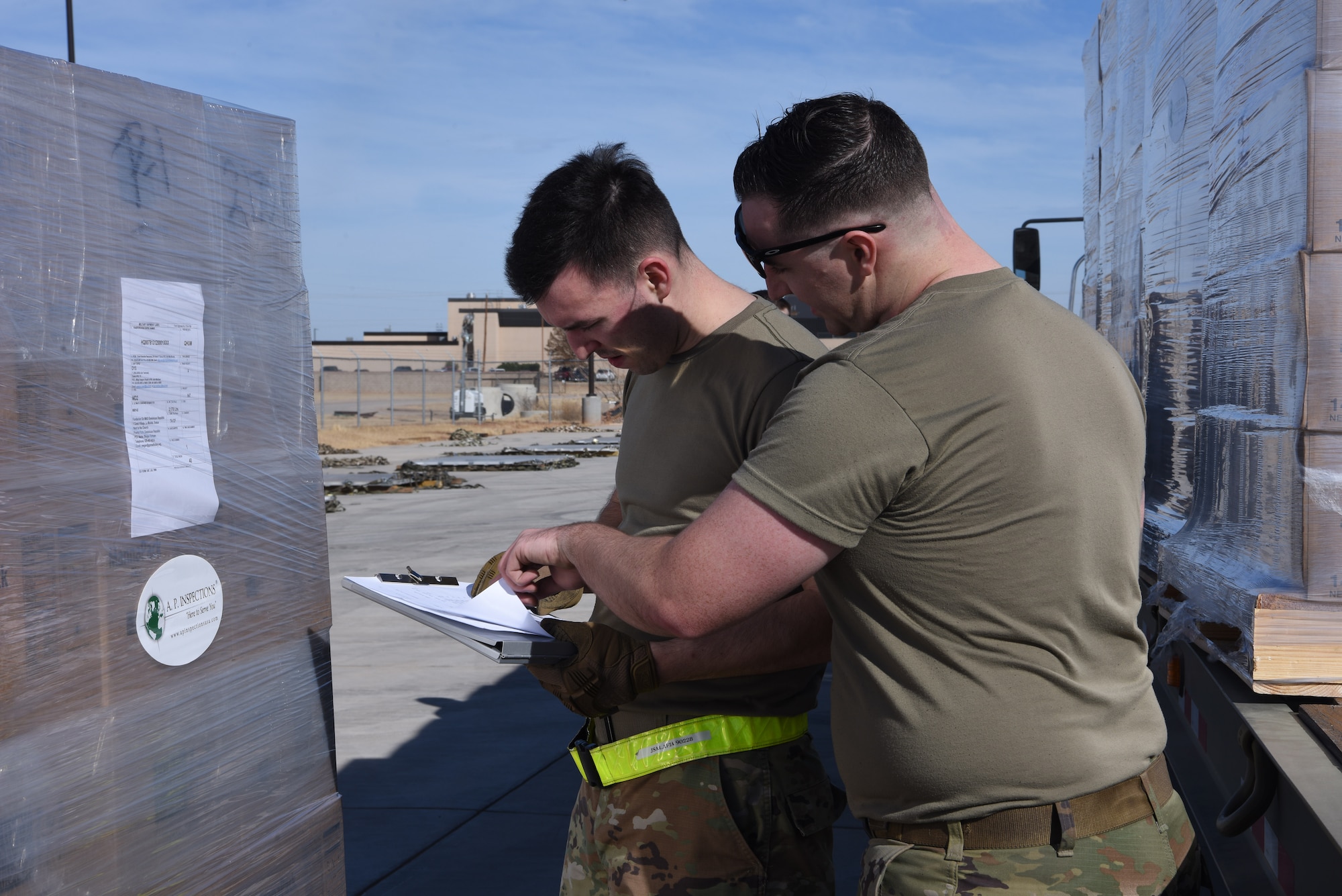 Photo shows two Airmen looking over a clipboard while standing next to a pallet.