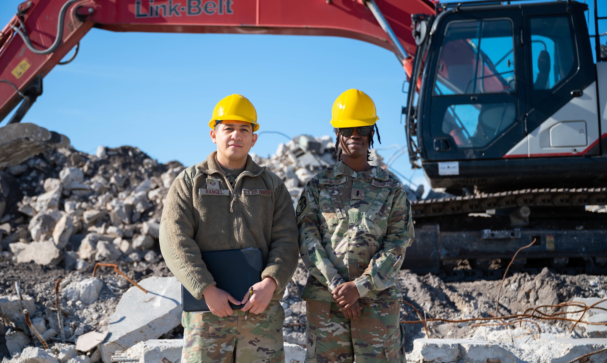 Two Airmen stand in front of rubble