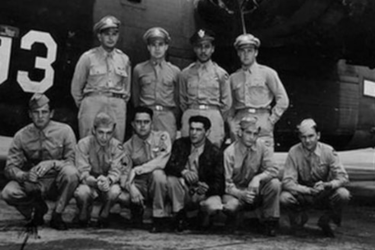 A group of service men in uniforms poses for a photo in front of an airplane on the tarmac.