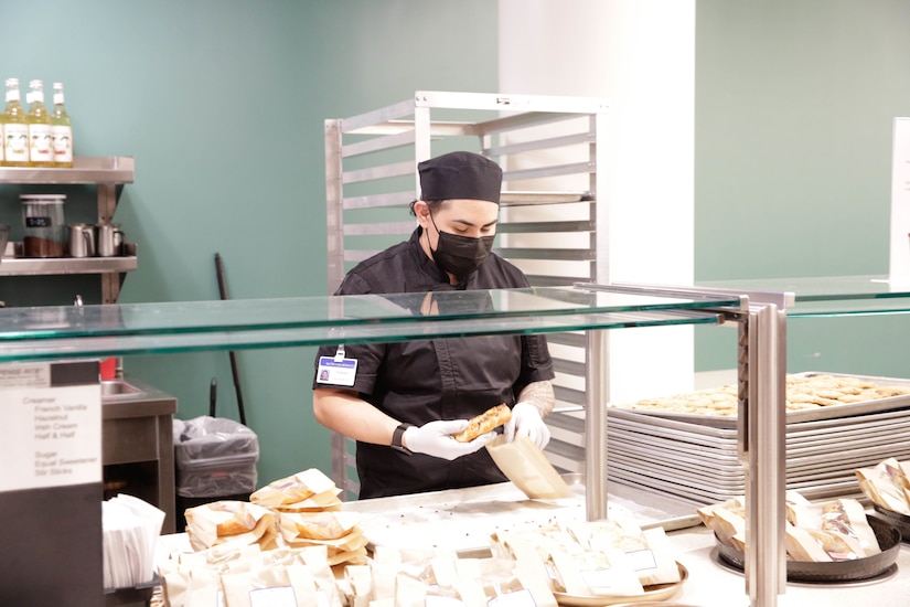 A soldier wearing food preparation clothing preps a meal