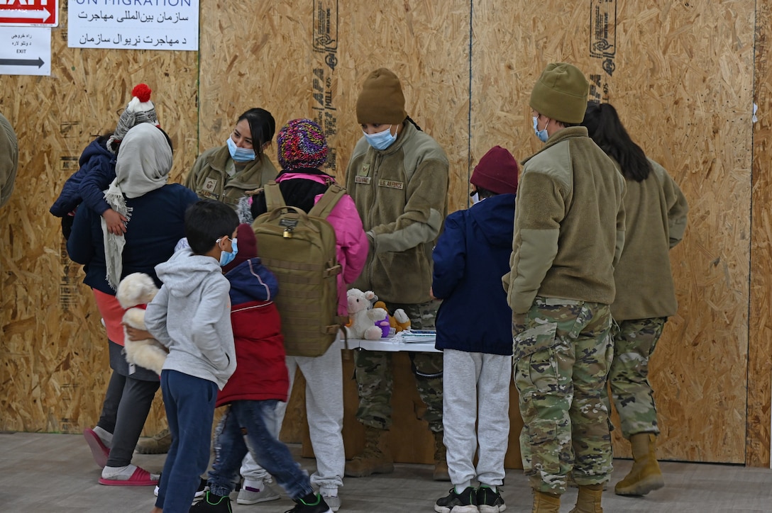 Two Airmen wearing face masks hand out stuffed animals to Afghan children.