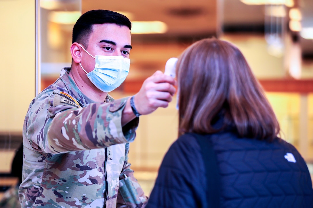 A soldier wearing a face mask performs a temperature check on a woman.