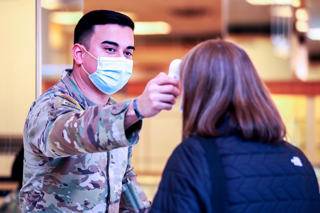 A soldier wearing a face mask performs a temperature check on a woman.