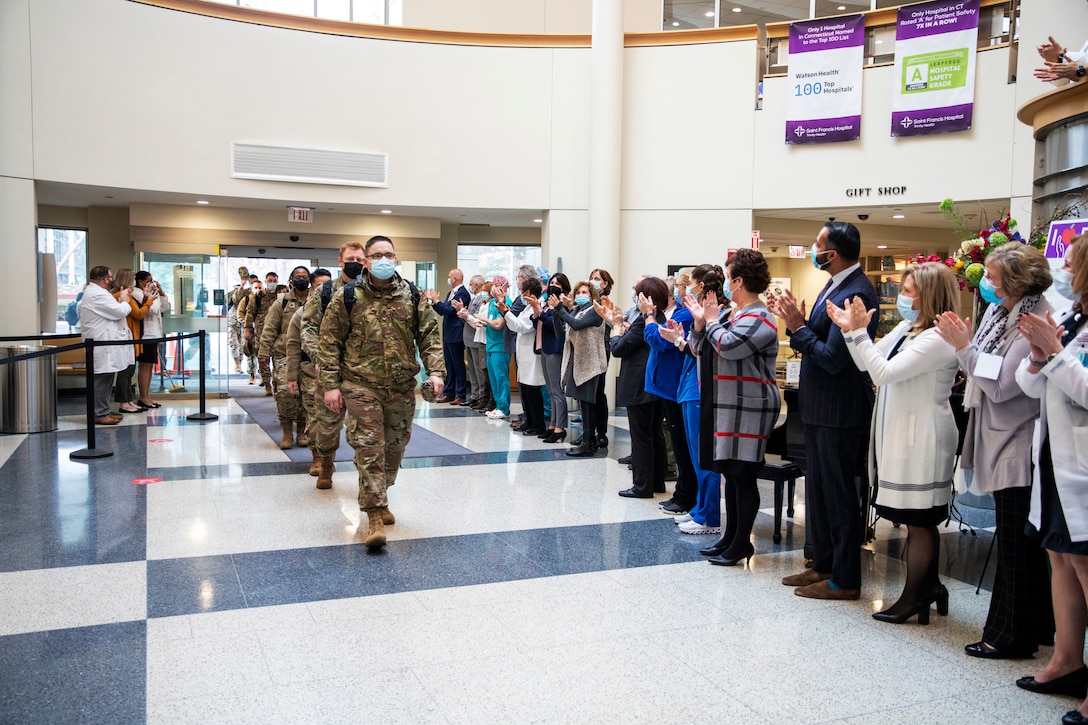 A team of soldiers wearing face masks arrive at a medical center while staff wearing face mask welcome them with applause.
