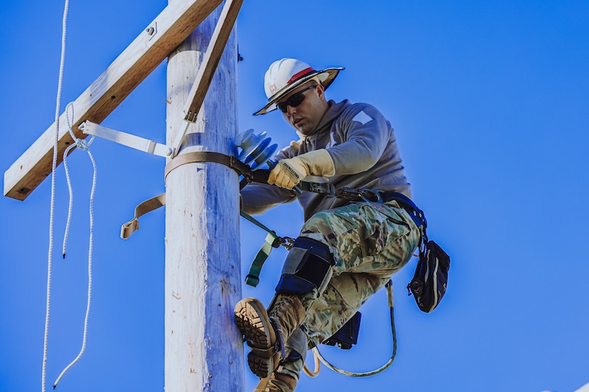 U.S. Army Soldier  at the top of a telephone pole completes lineman work.