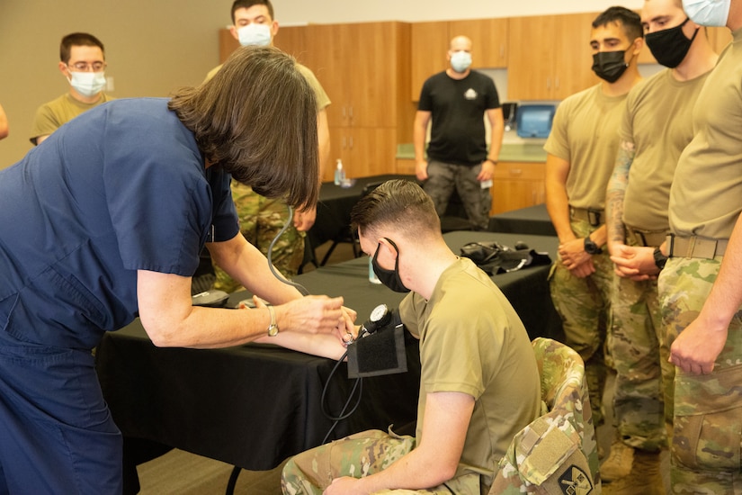 A nursing instructor puts a blood pressure monitor on a soldier's arm