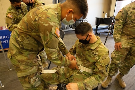 Soldier ties a strap around a seated soldier