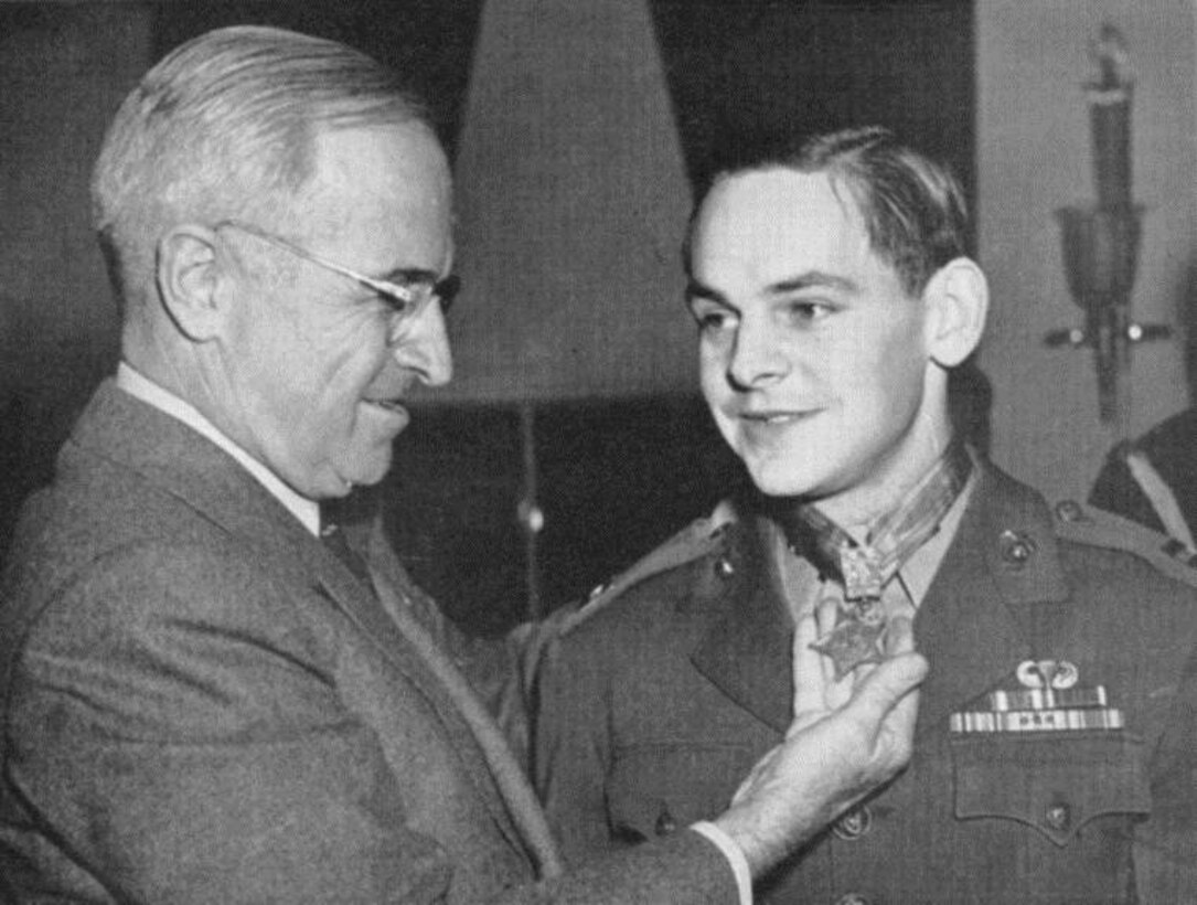 A man holds a medal in his hand that’s around the neck of another man.