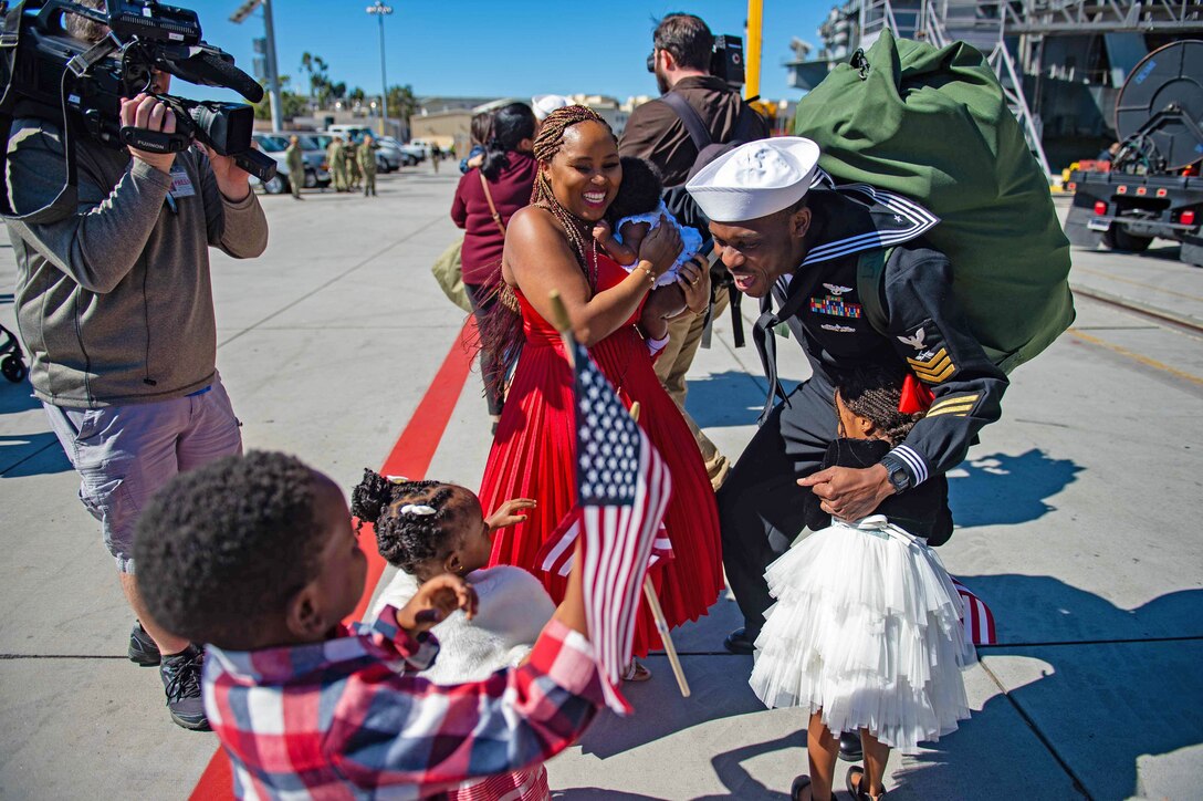 A videographer films as a sailor reunites with his family on a pier.