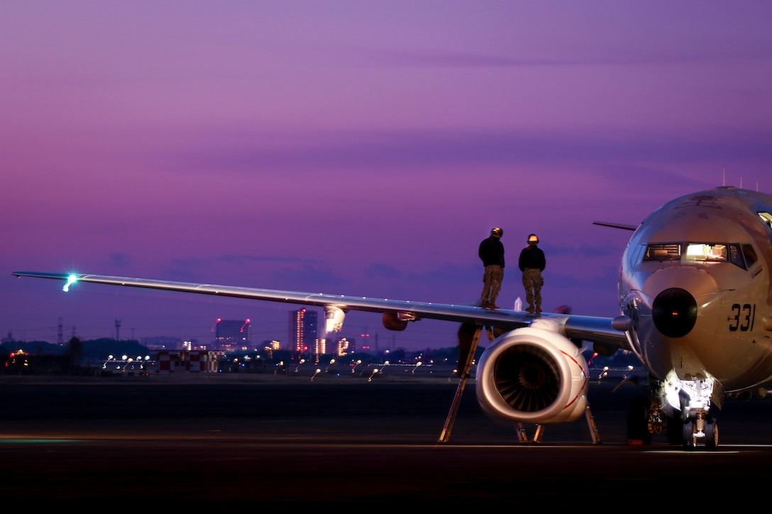 Sailors stand on the wing of an aircraft under a purple sky.