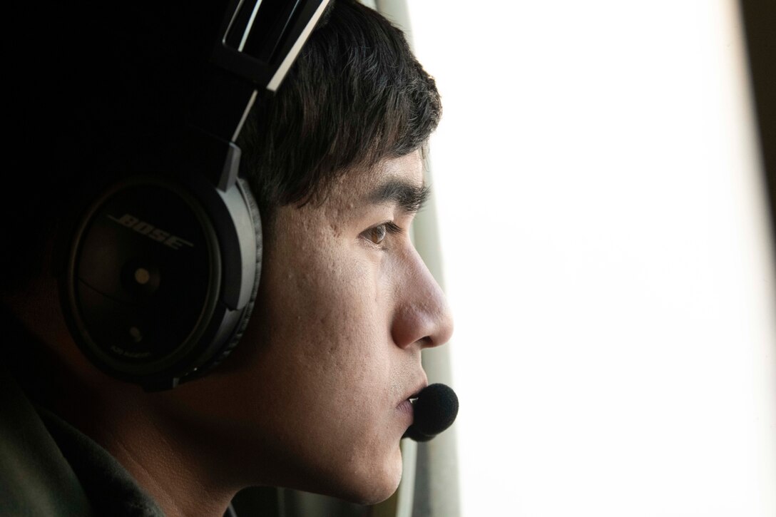 A Marine wearing headphones looks out of an aircraft window.