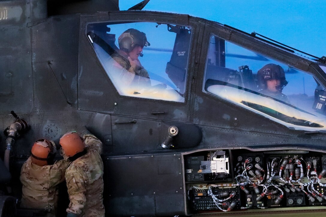 Two soldiers work on a helicopter as two others sit in the cockpit.