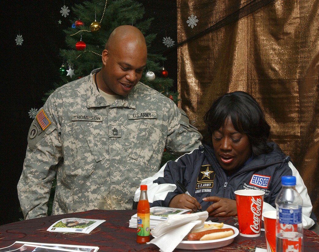 A woman signs an autograph for a soldier.