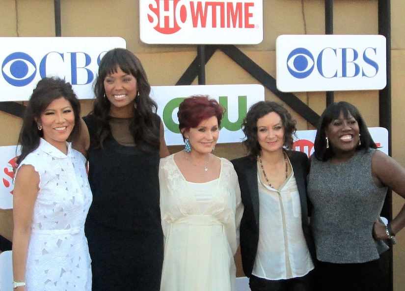 Five women pose for a photo in front of media company signs.