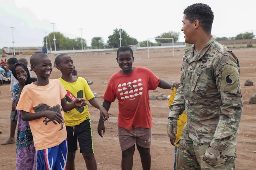 A soldier and some kids laugh together while standing outside.