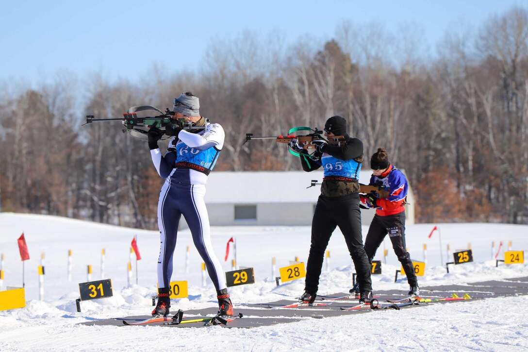 Two men on skis prepare to shoot their guns while a third loads her gun.