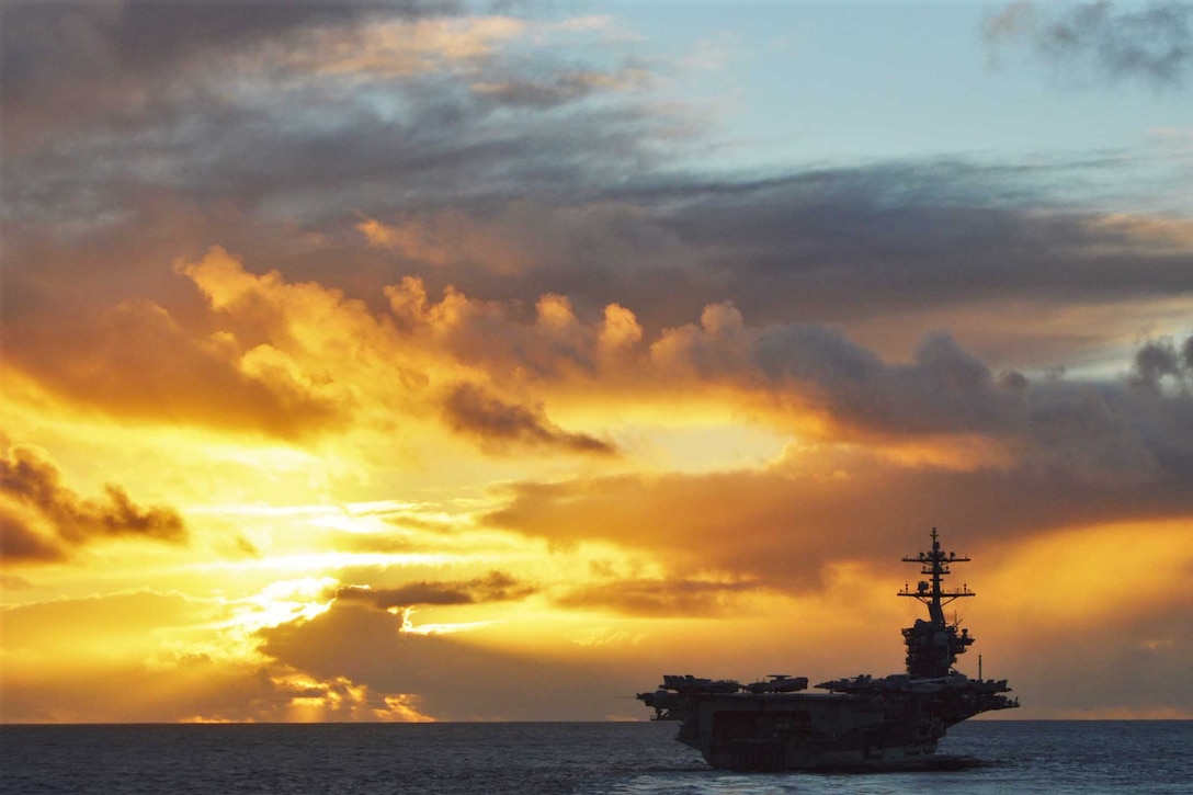 An aircraft carrier sails on the ocean at twilight.