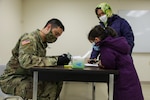 U.S. Army Reserve Staff Sgt. Christopher Michon, left, assigned to 773d Transportation Company, Fort Totten, New York, verifies an Afghan evacuee’s information during winter gear distribution at Fort McCoy, Wisconsin, Dec. 13, 2021.