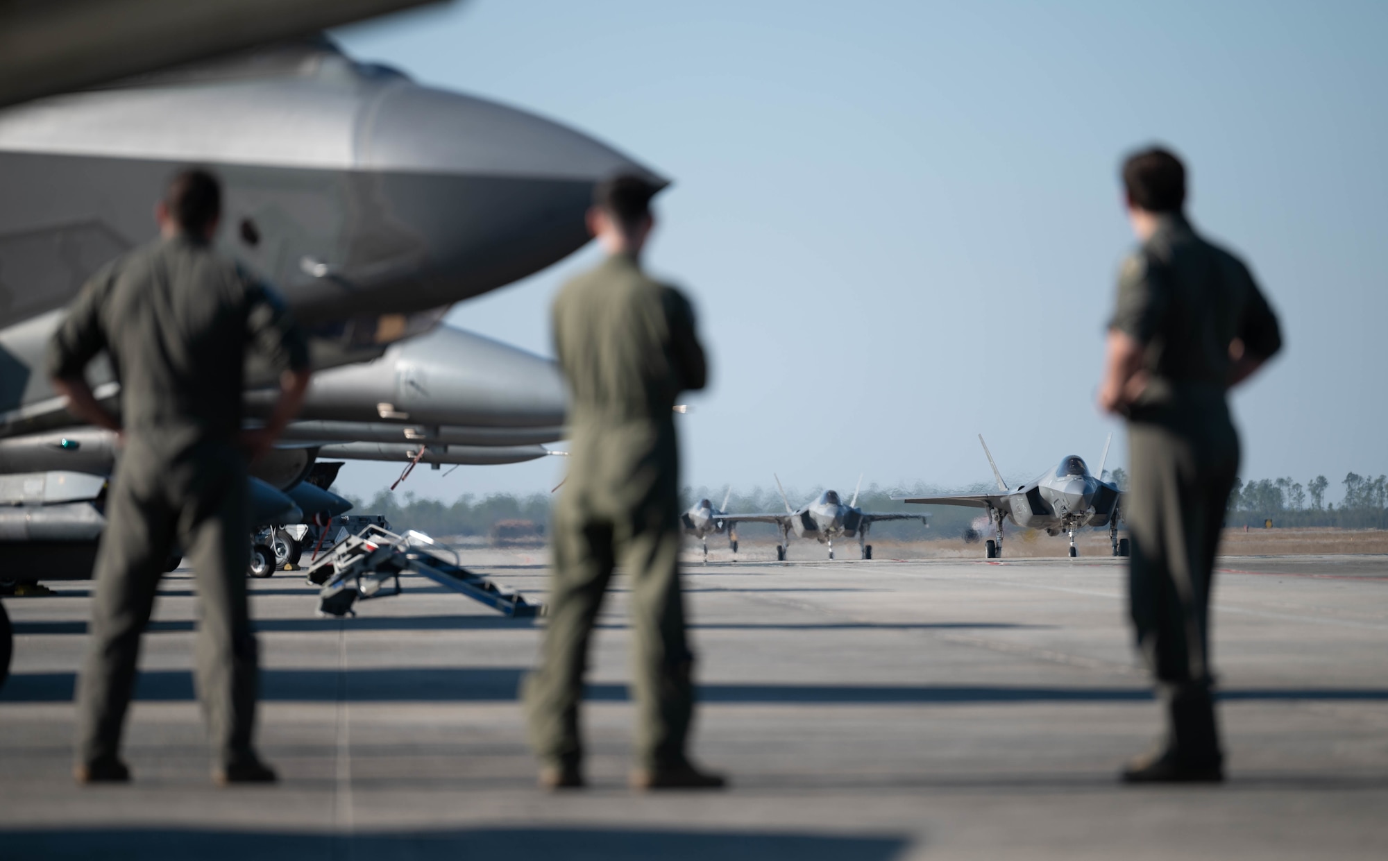 Airmen watch F-35A Lightning IIs taxi on the flight line.