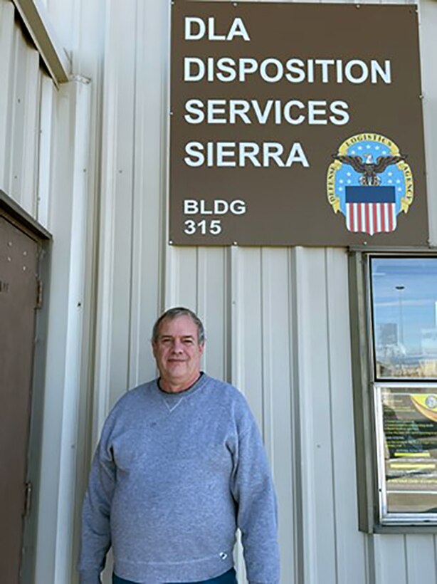 A man posing in front of a building sign.