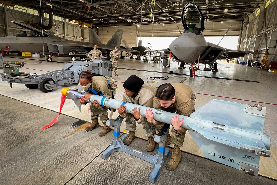 Three airmen lift a missile.