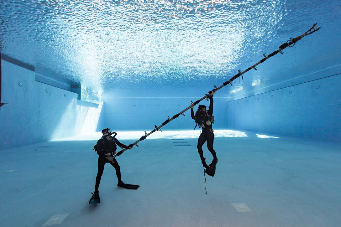 Two divers raise a ladder in a large swimming pool.