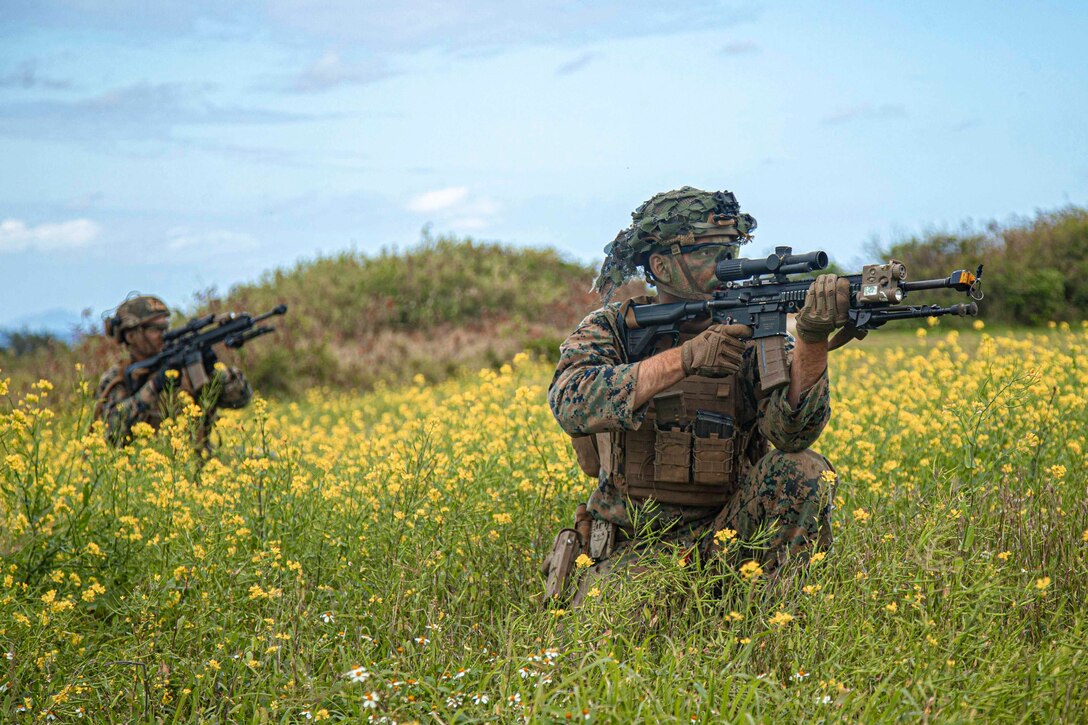 Two Marines move through a grassy area holding weapons.