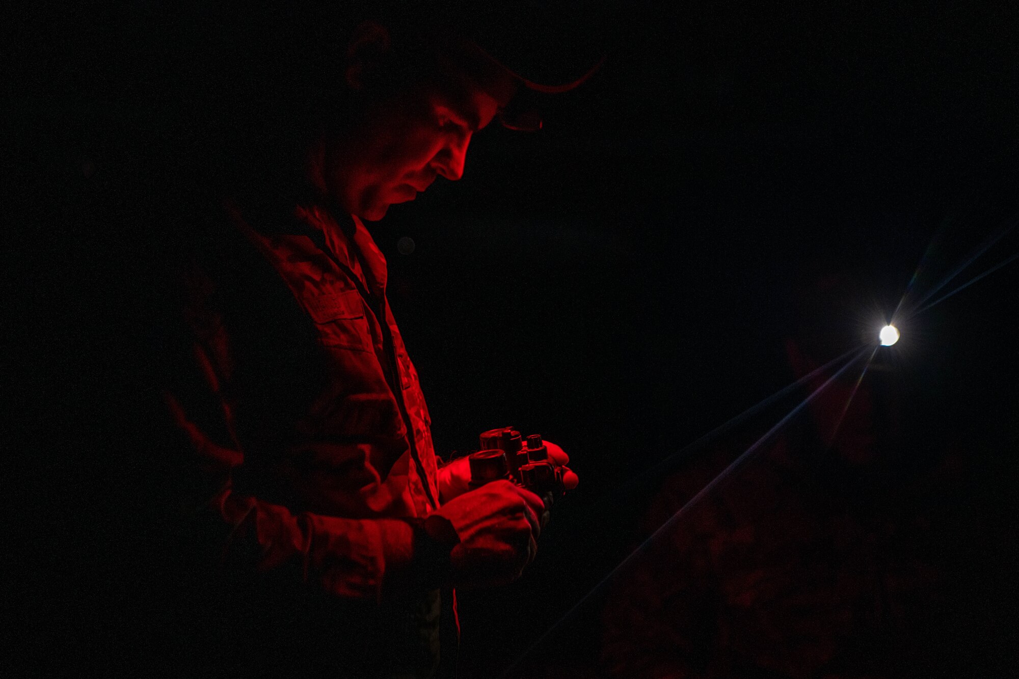 man in red light looks at NVGs