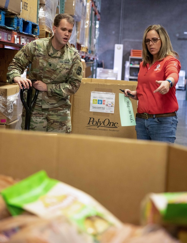 A soldier and a woman look at packaged food in a large box