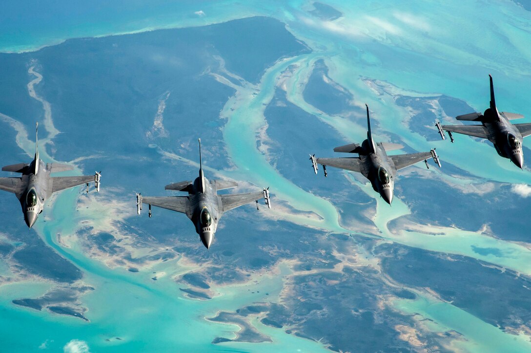 Four aircraft fly next to each other over turquoise waters and landscape.