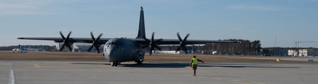 An airman guides a large aircraft on the tarmac.