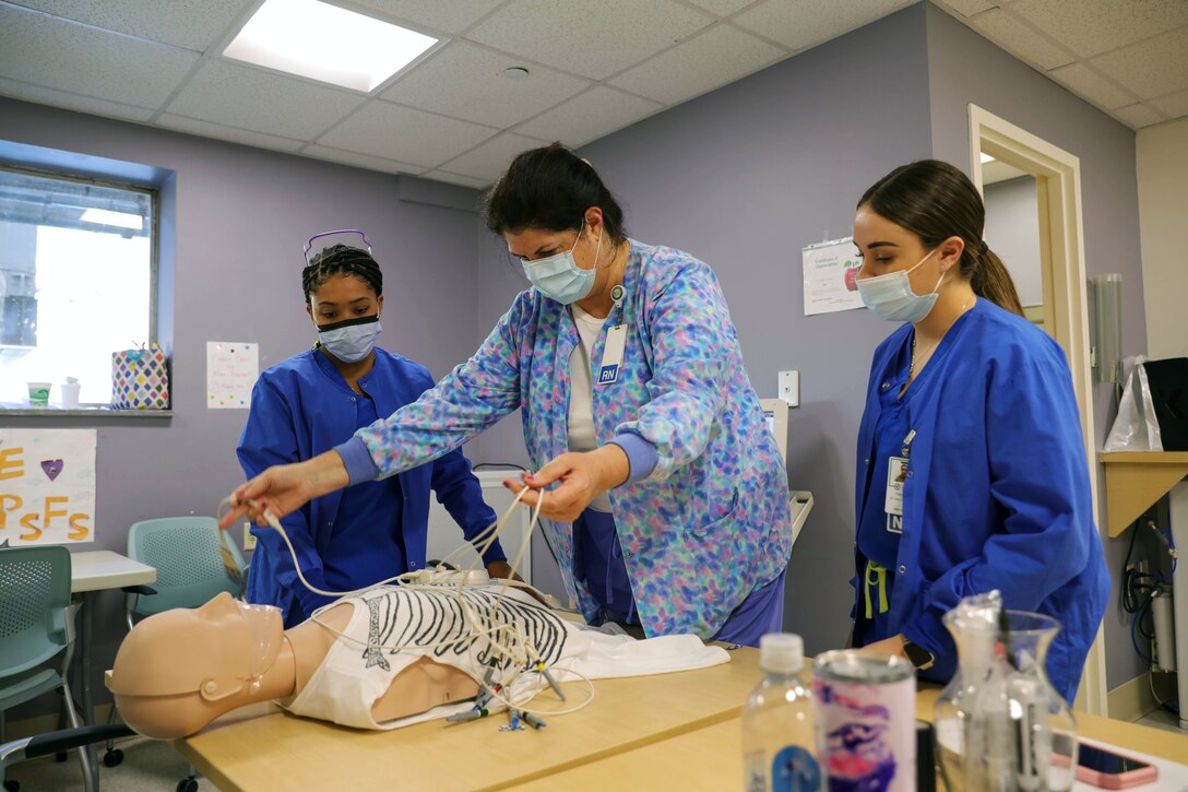 Two airmen wearing face masks receive electrocardiography training from a medical instructor wearing a face mask at Lawrence General Hospital.