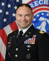 man in army uniform standing in front of two flags.