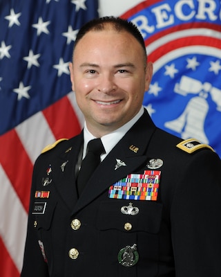 man in army uniform standing in front of two flags.