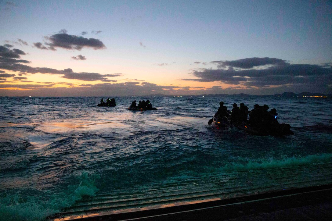 Marines ride in three small inflatable boats through waters.