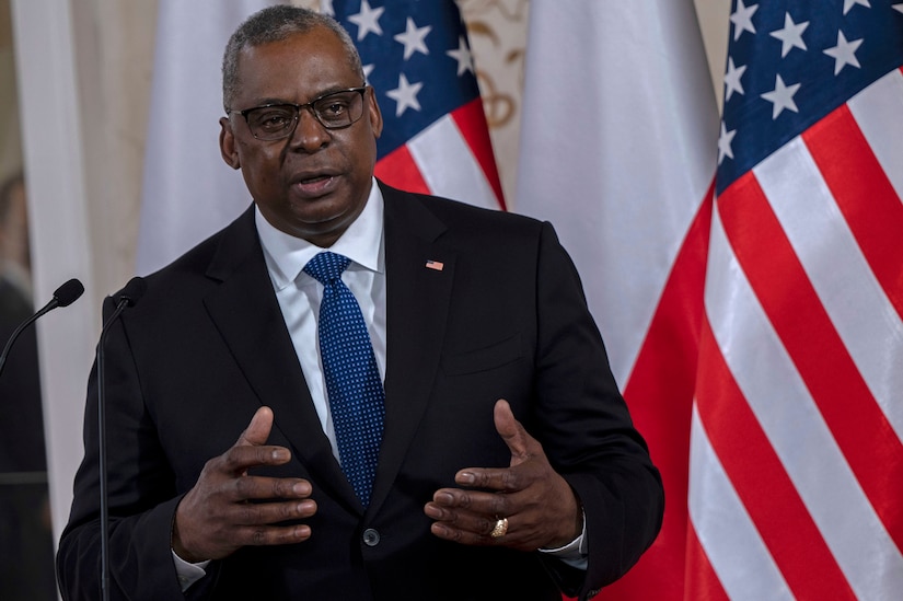 Secretary of Defense Lloyd J. Austin III speaks in front of American flags.