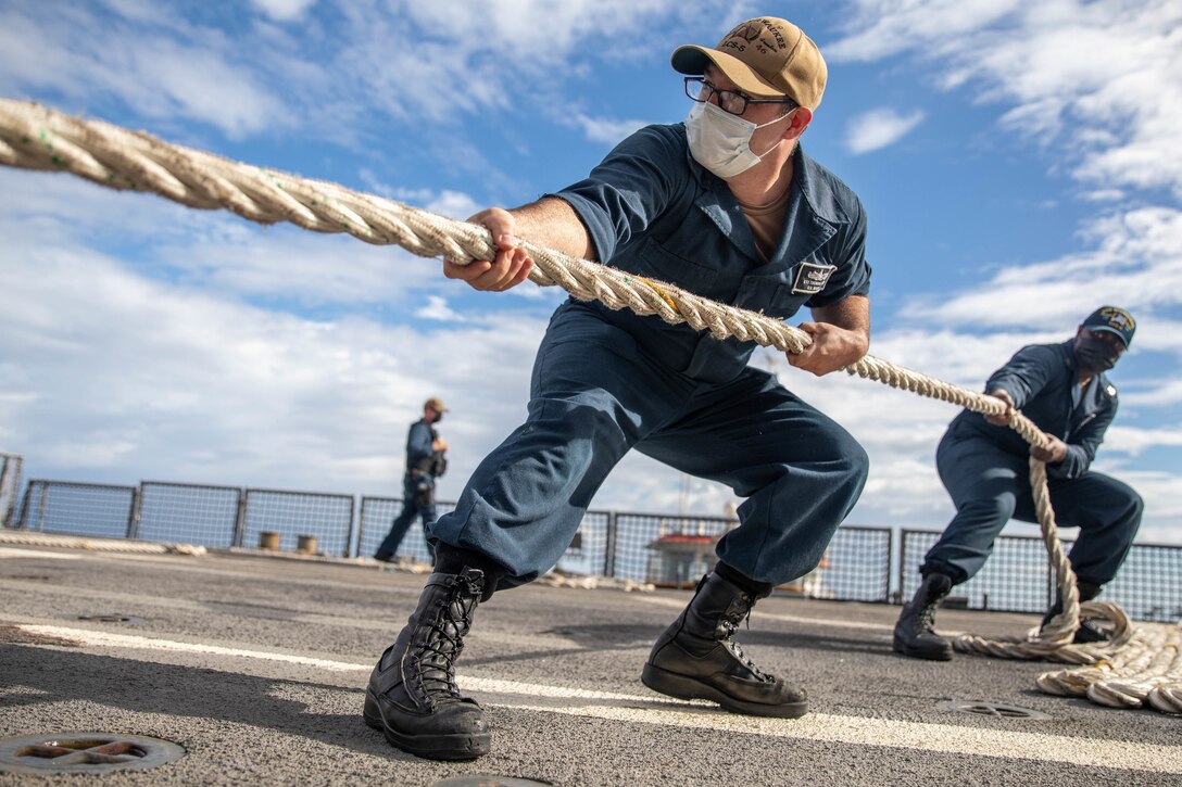 Two sailors pull a thick rope on board a ship.