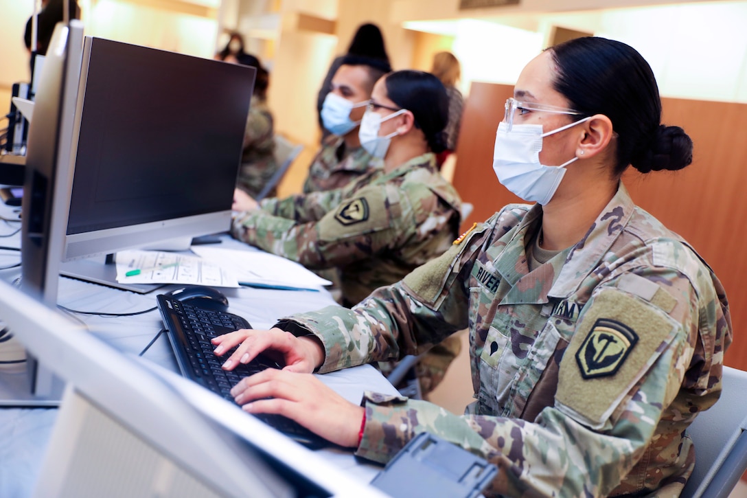 Several soldiers wearing face masks and sitting in front of computers add patients’ information.