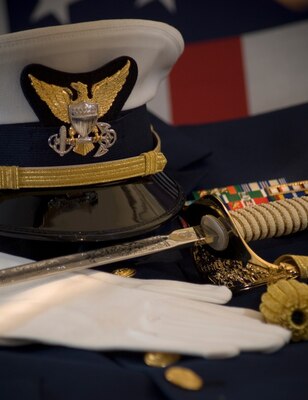 A Coast Guard Officer's hat, sword, gloves and ribbons are displayed together with the American Flag.