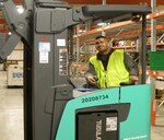 A man poses on material handling equipment in a warehouse.