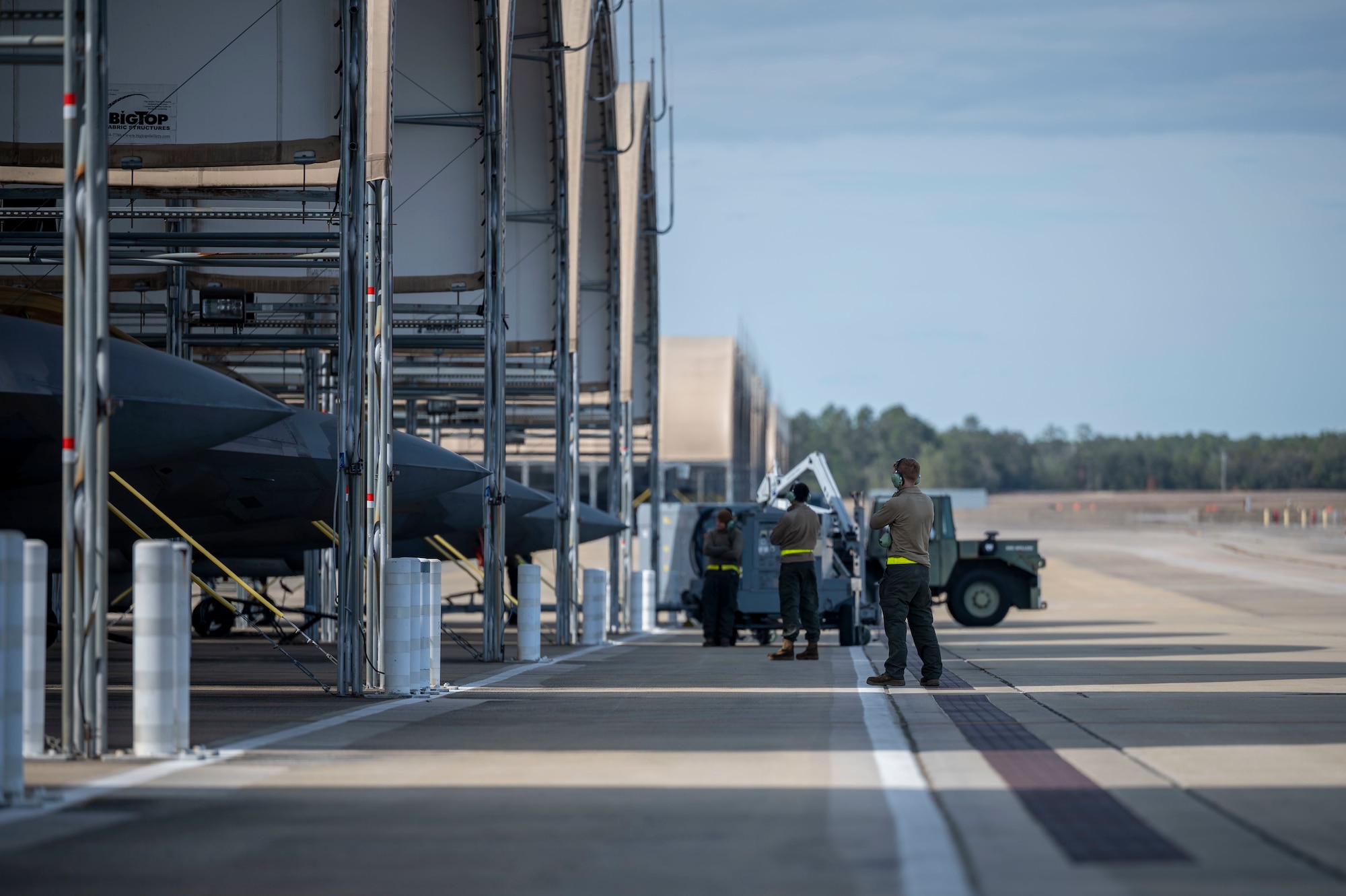Three crew chiefs signal a holding sign to aircraft pilots