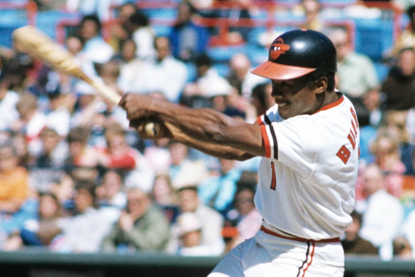 A baseball player swings a bat while wearing a Baltimore Orioles uniform.