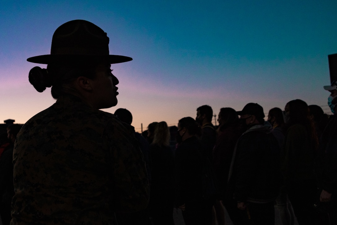 A Marine speaks to a group of people at twilight.