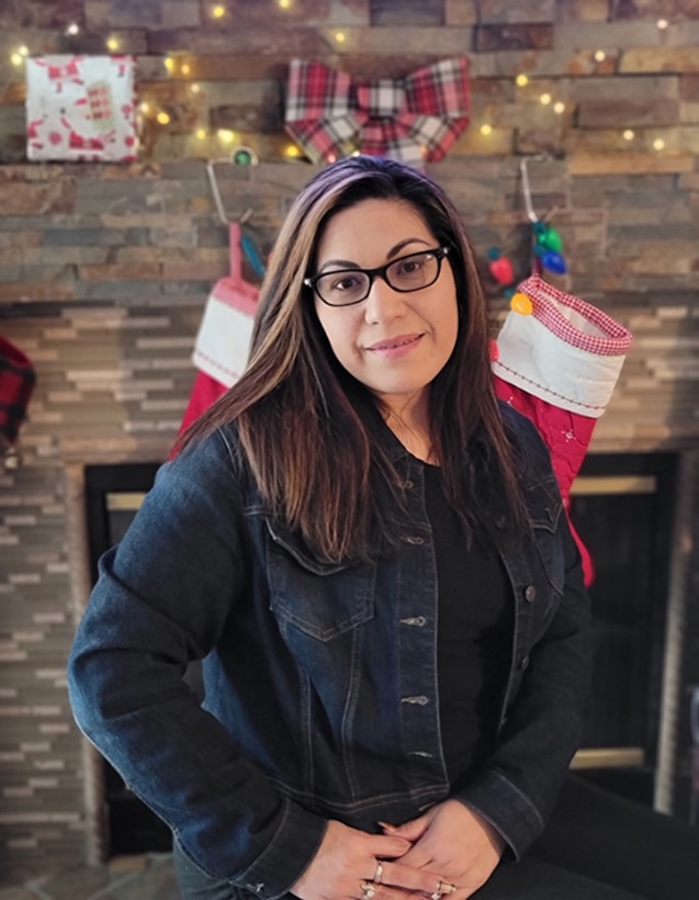 A woman poses in front of a fireplace.