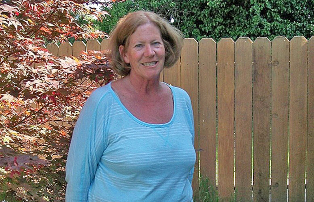 A woman poses in front of a wooden fence.