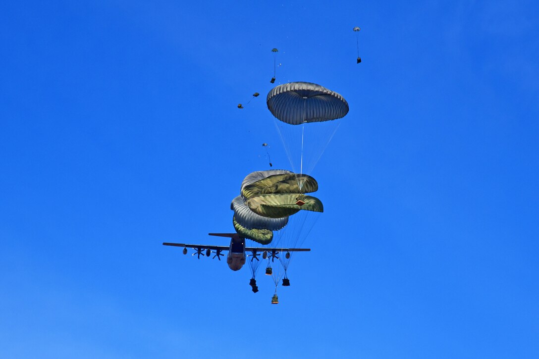 Packages are parachuted to the ground from a large military aircraft.