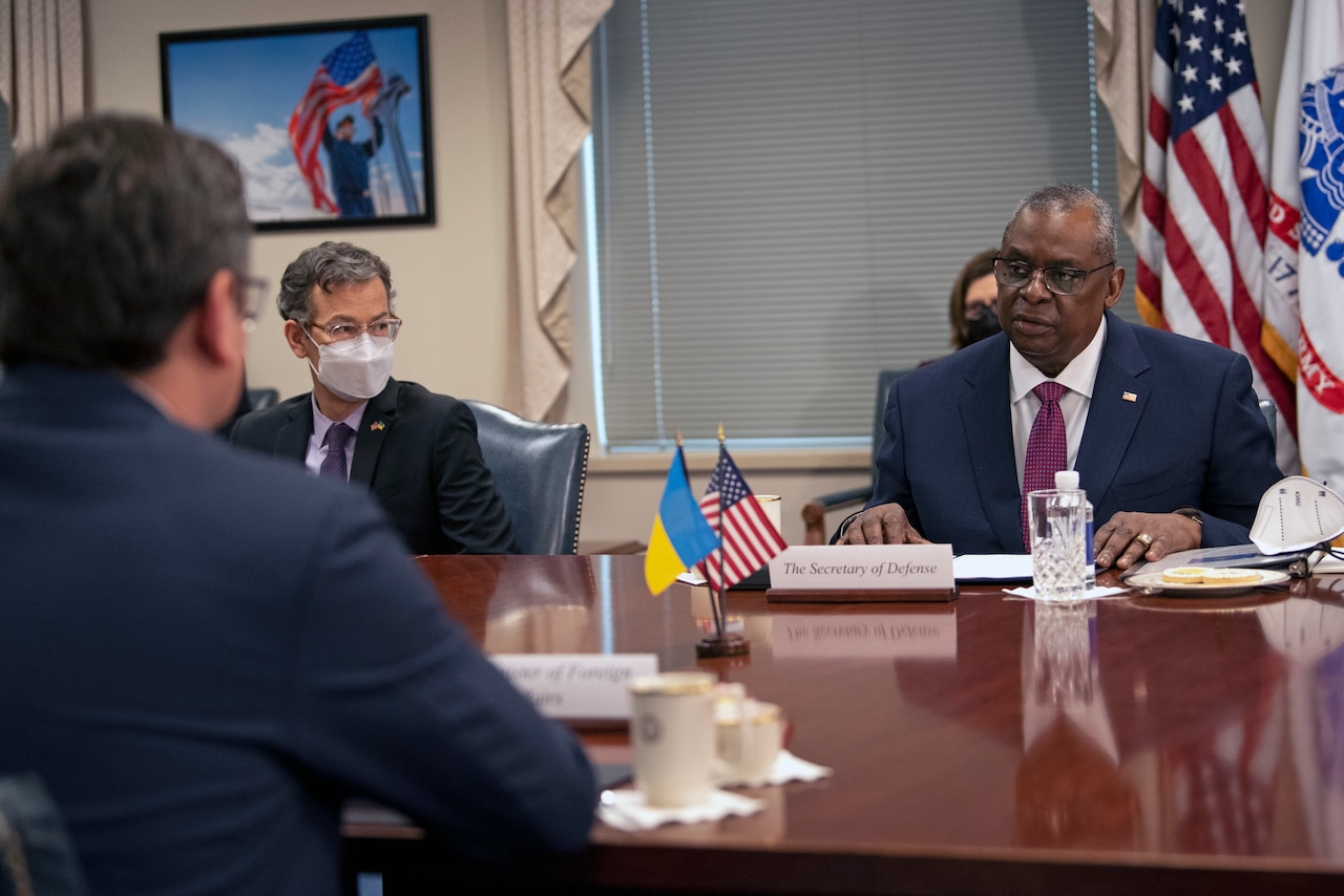 Two men converse across a table from. Small flags are in the center of the table.